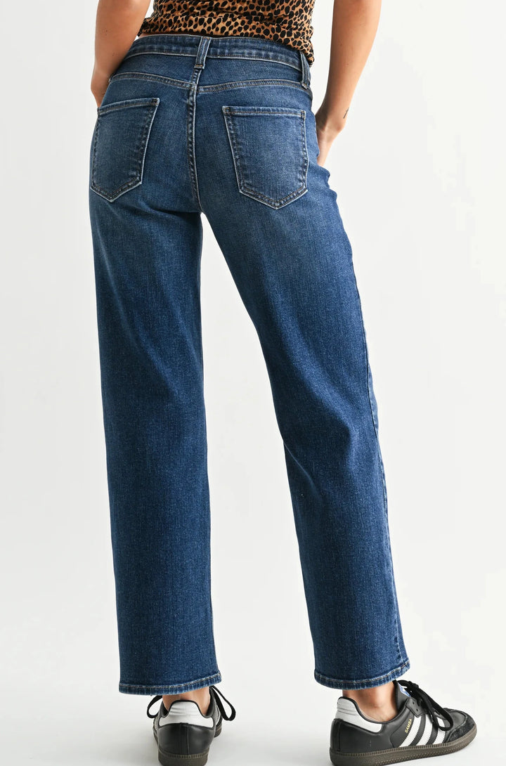 A model wearing a pair of medium-wash blue straight-leg jeans, styled with a leopard-print top and black sneakers, photographed against a light gray studio background, facing backwards.