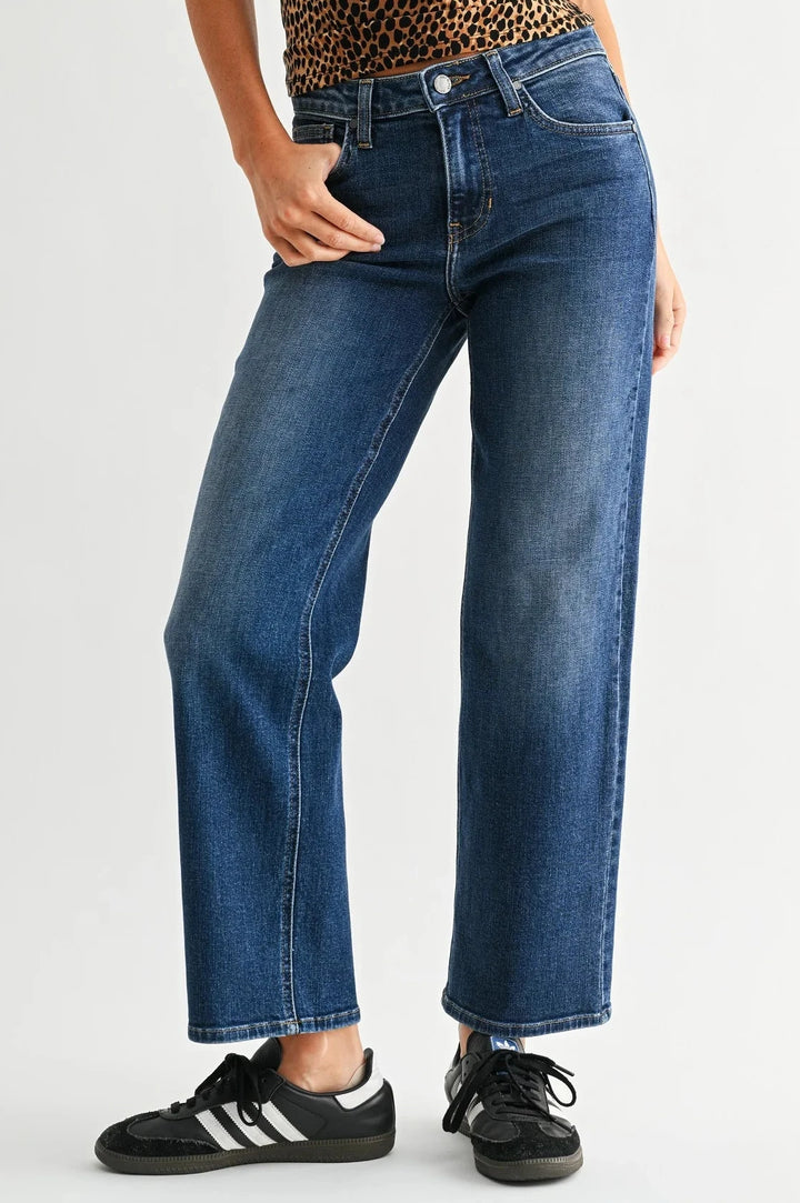A model wearing a pair of medium-wash blue straight-leg jeans, styled with a leopard-print top and black sneakers, photographed against a light gray studio background.
